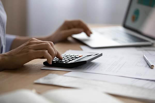 Cost calculation at a desk. Hand on a calculator and computer in the background. 