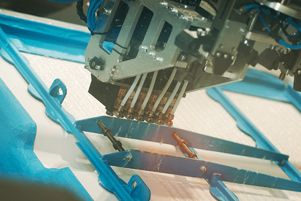 An Aero spray head with six spray elements is applying PUR adhesive on a battery cover.
