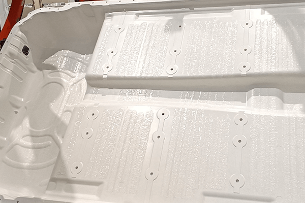 A three-dimensional sheet of a white battery cover with rows of swirl-tpye adhesive application. 