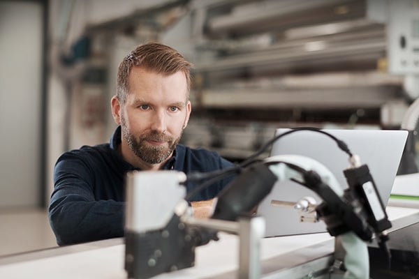 A person checks whether the bead application with hot melt adhesive meets the quality requirements: clean cut-off, application to the defined position, correct adhesive quantity. 
