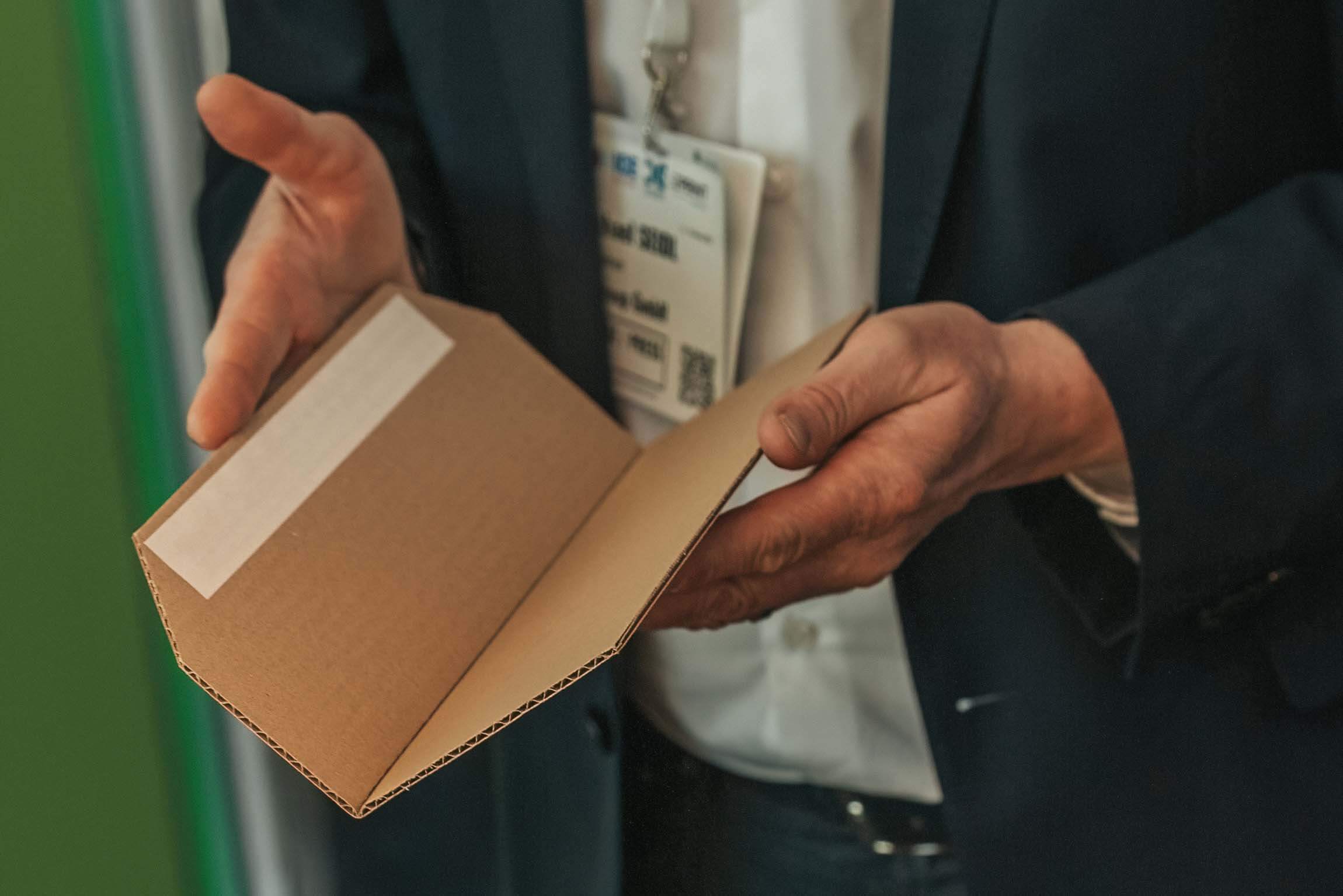 Odwiedzający targi CCE 2023 w Monachium trzyma w dłoniach tekturę falistą złożoną za pomocą płynnej bigówki PerfectFold.